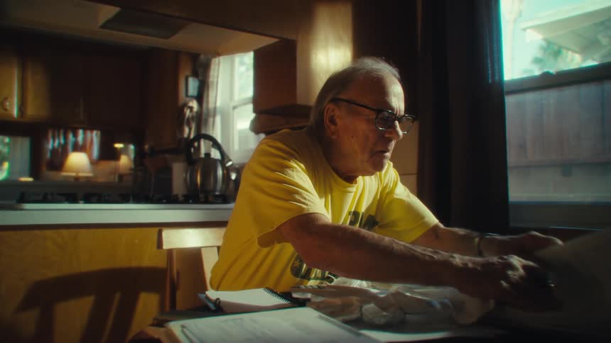 Elderly man in a veteran shirt organizes papers on the kitchen table