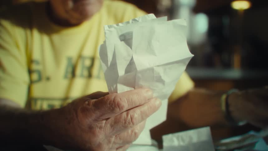 A closeup of a man wearing a yellow shirt and glasses as he smiles and laughs while he is gathering receipts