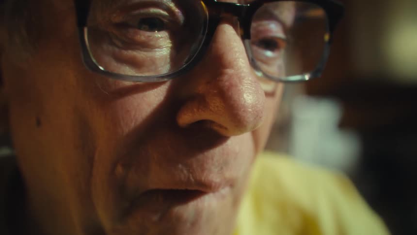 Elderly man with glasses smiles in a brightly lit closeup