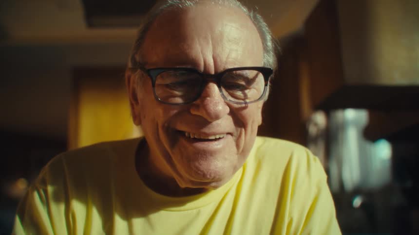 An older man with glasses looking at a smartphone with concentration before breaking into a genuine joyful laugh