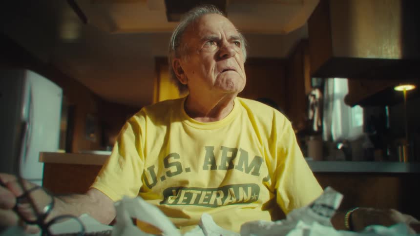 An elderly man at a table looking frustrated and stressed as he tears and crumples up papers