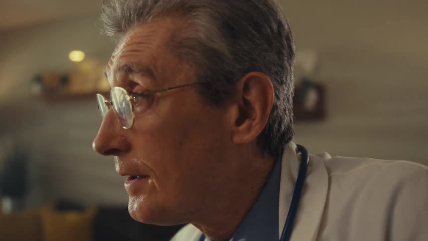 A doctor wearing a white coat and stethoscope seated indoors