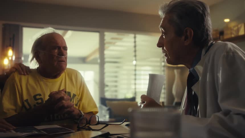 Elderly man in a veteran shirt talks with a doctor beside his wife