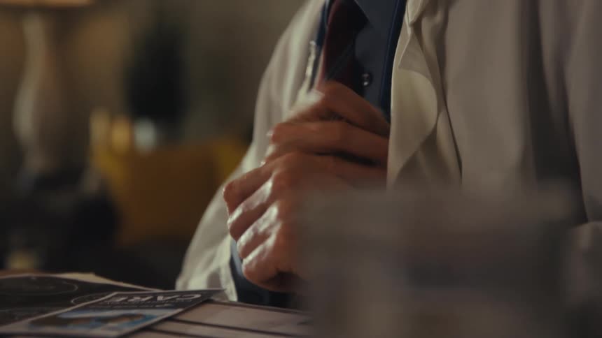A doctor in a white coat with a stethoscope around his neck smiles as he takes a pen out of his pocket