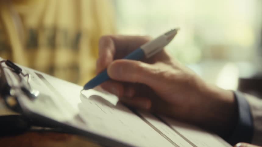 An elderly man sits in a doctors office while the doctor writes on a notepad at midday