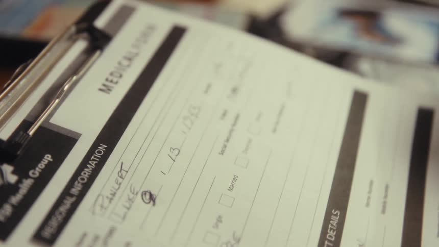 A close view shows a persons hand turning over the page of a medical form on a clipboard