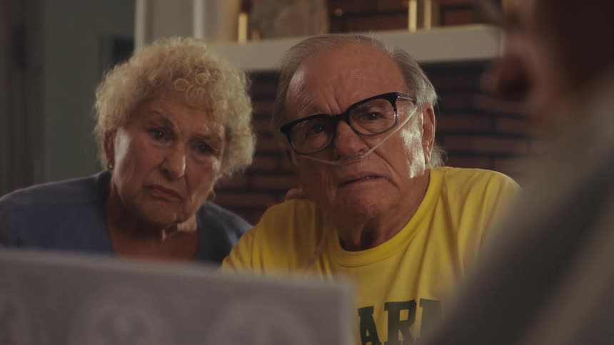 An elderly couple looks worried as a doctor shows them medical reports at home