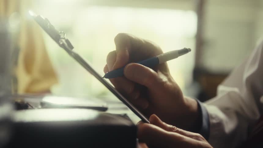 In this closeup shot a persons hand is seen holding a clipboard and a pen they are in the process of writing on the clipboard