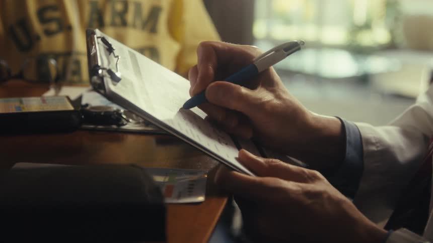 Close up of a doctor filling a patients document on a clipboard at a table in a room during daytime