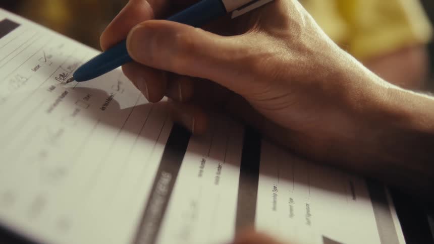 A close view of a persons hand writing on a medical form on a clipboard with a blue pen