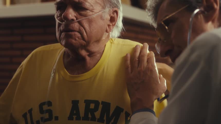 A doctor is examining an elderly patient who is wearing a nasal cannula using a stethoscope
