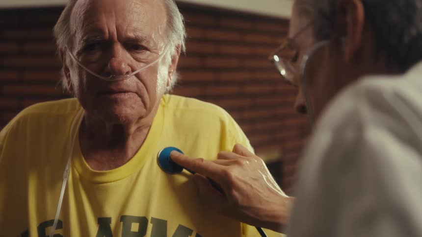 Elderly man with nasal oxygen is examined by a doctor with a stethoscope