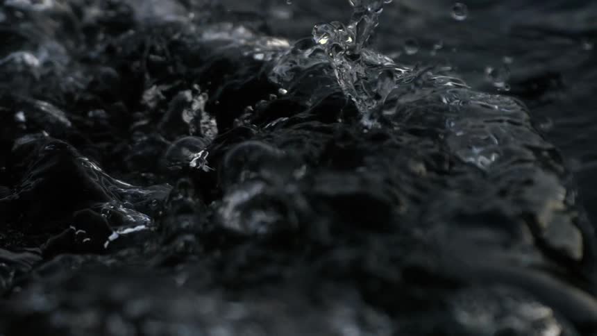 A small wave on a dark liquid with a reflective surface with large drops of it splashing and bubbling