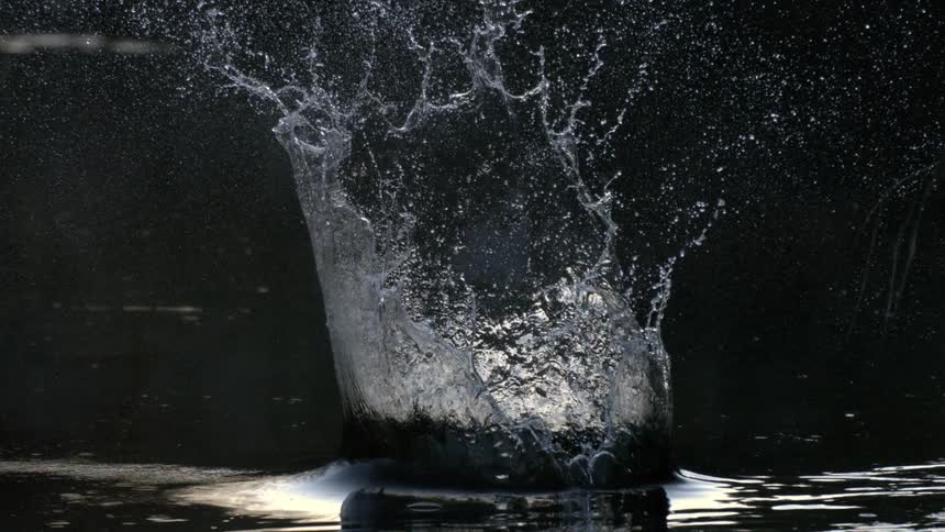 Object hits the water surface creating a splash in a dark setting
