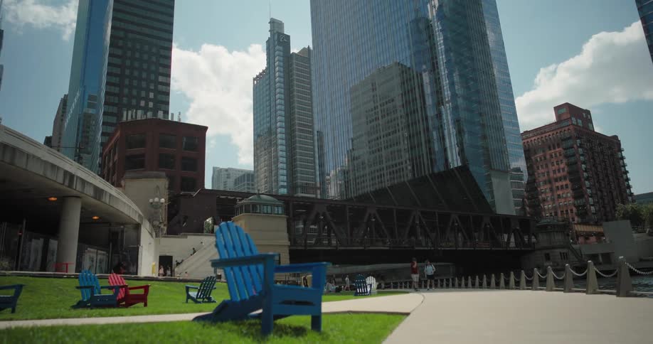 Colorful chairs on a riverside lawn with skyscrapers reflecting the sky in the background