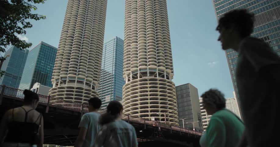 People walking by in front of a tower block including two cylindrical skyscrapers