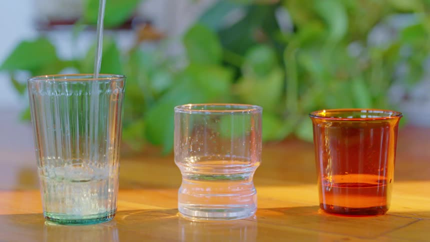 Three glasses are lined up and water is poured into one at a time
