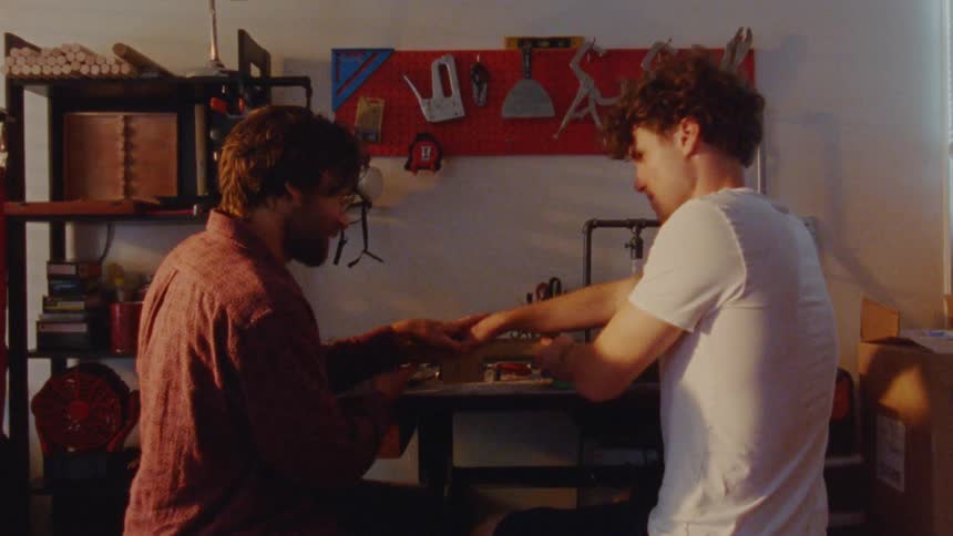 Two men sit in a workshop sharing a friendly moment