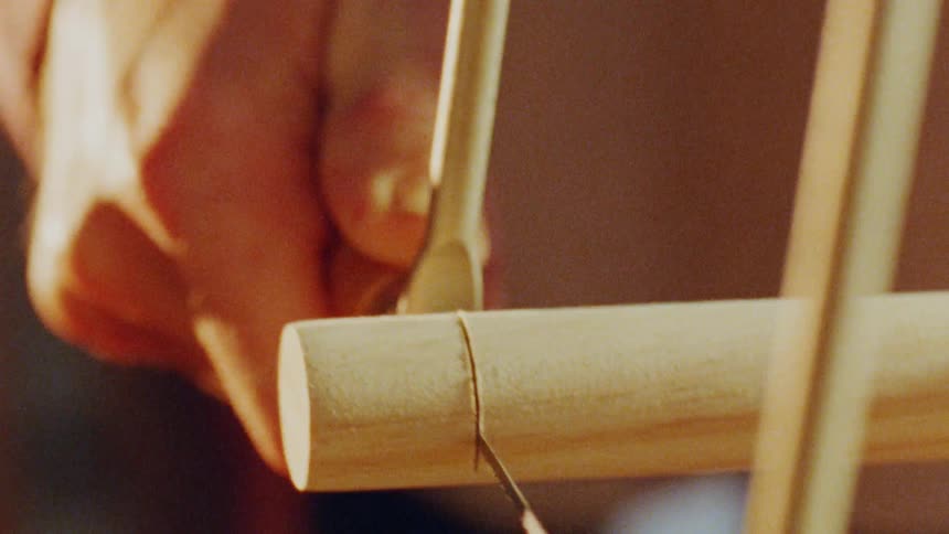 A person uses a wire saw to cut off then end of a wooden rod