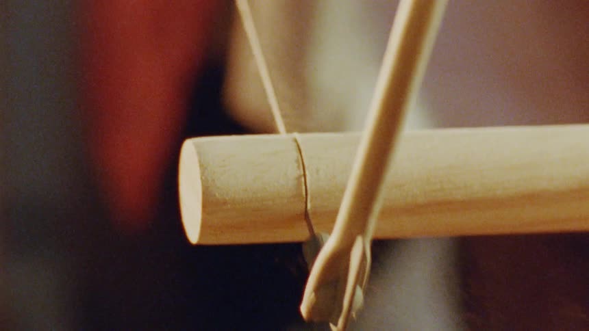 A thin wire saw slices through a smooth wooden dowel