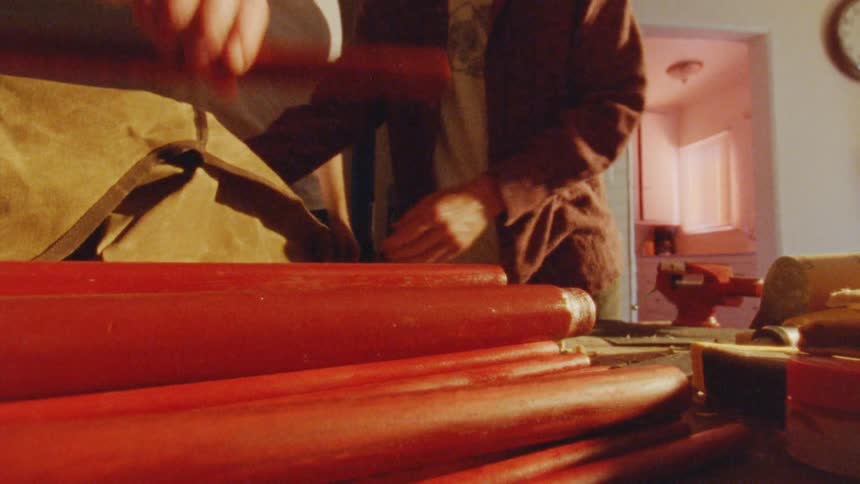 People hold a red cylindrical object over a table full of similar items and store it inside a bag