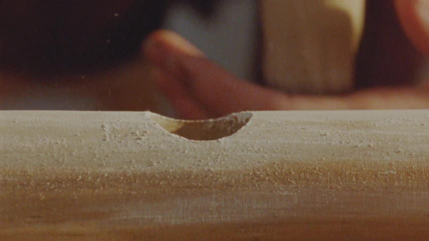 A carpenter tries to fit a piece of wood into a hole drilled in another piece blowing off the excess wood from the hole