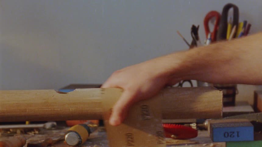 Hands work together sanding a piece of wood on a workbench