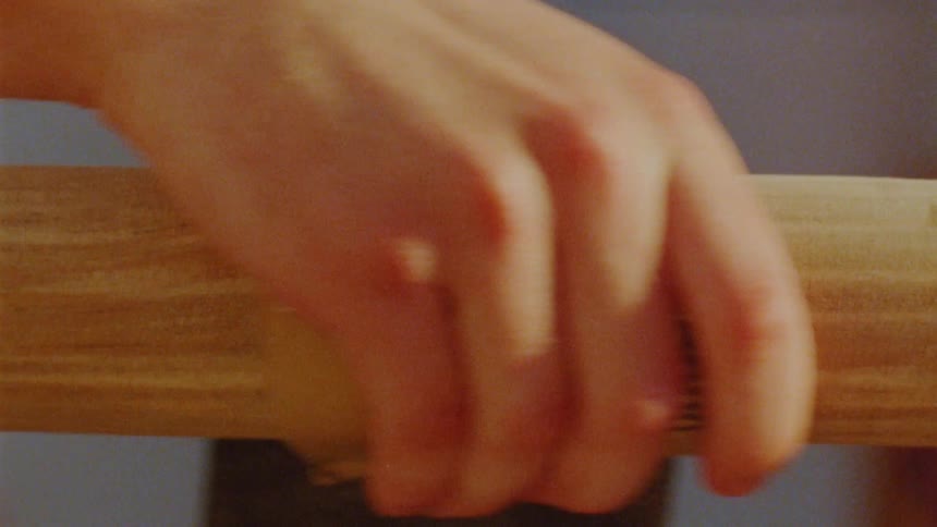 A persons hand firmly grips sand paper to sand a wooden handle in warm lighting