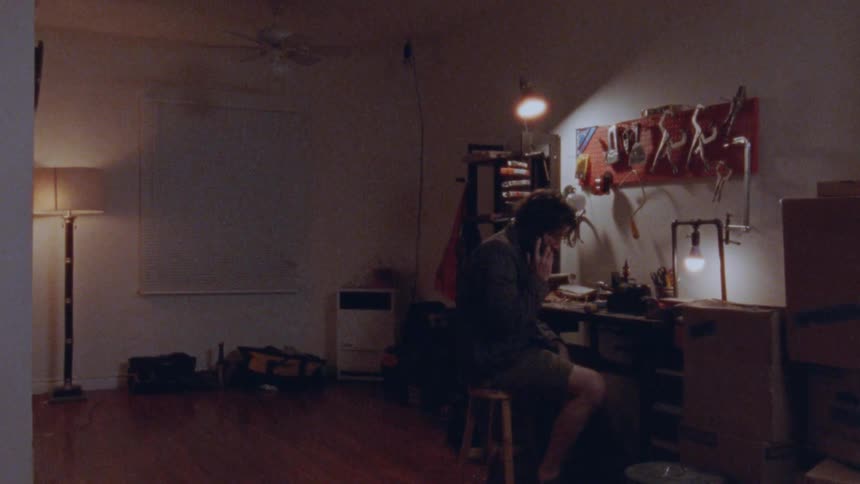 A man sitting at a workbench picks up a phone call on his cell phone