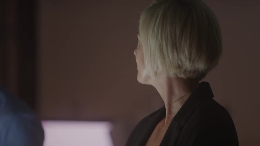 Shorthaired blonde woman smiles subtly in a softly lit setting
