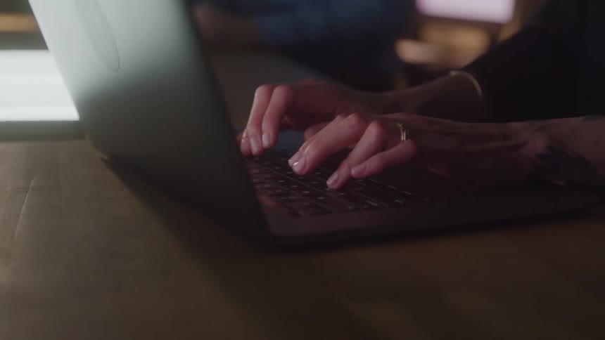 Hands typing on a laptop keyboard in a dimly lit setting