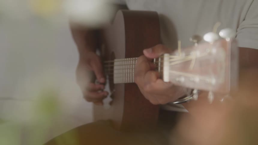 Hands strum the strings of an acoustic guitar in a softly lit setting