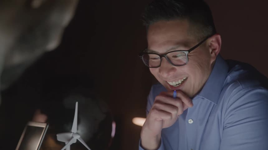 Smiling man looks at a wind turbine model on the table