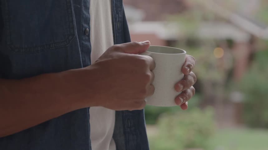 A close view of a person with a dark blue jacket and a white shirt shows them holding a white mug with both hands