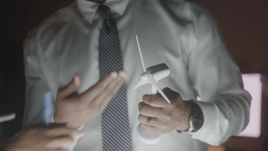 Hands hold a miniature wind turbine model during a discussion