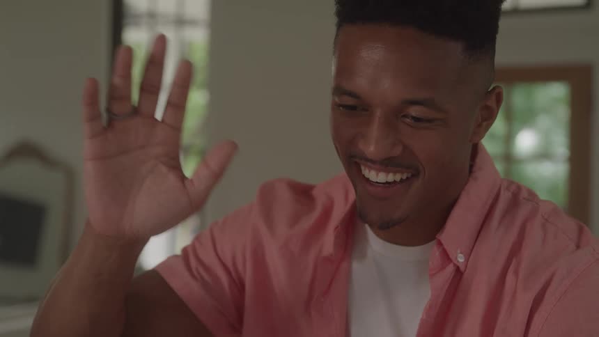 A young man smiles and waves while having a video call indoors