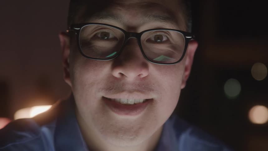A close view shows a man with dark hair and glasses looking directly into the camera with a smile