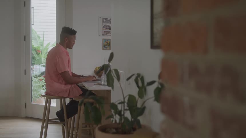Young man sitting on a tall stool typing on a laptop indoor