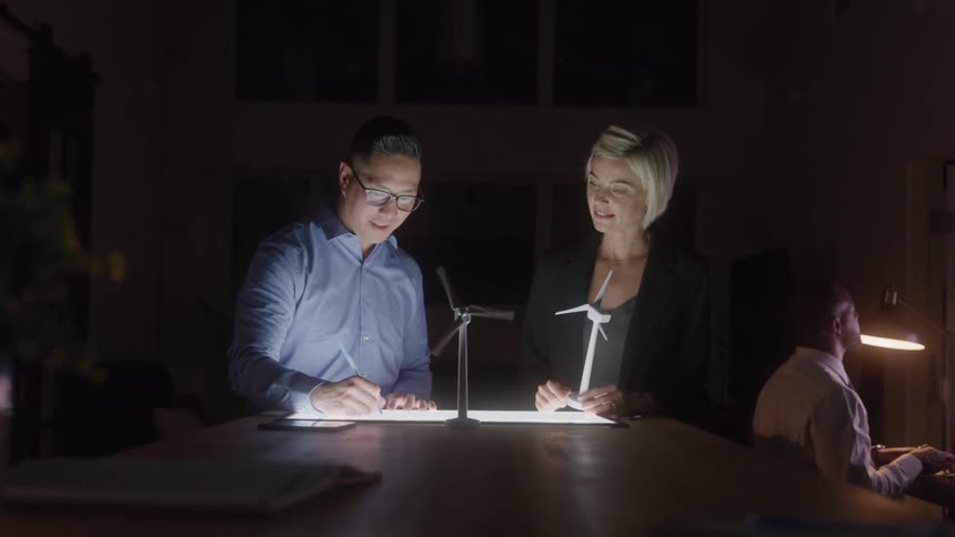 Two colleagues discuss a wind turbine project in an office
