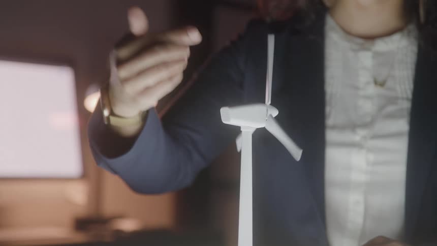 The video shows a closeup of a persons hands holding a small white wind turbine model the persons fingers gently spin the blades of the turbine suggesting a discussion about renewable energy or a related project
