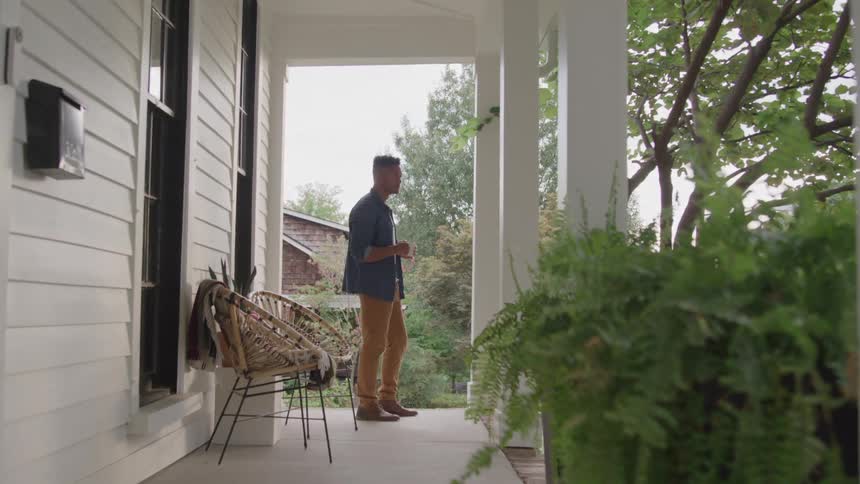 A man stands on a porch holding a coffee cup