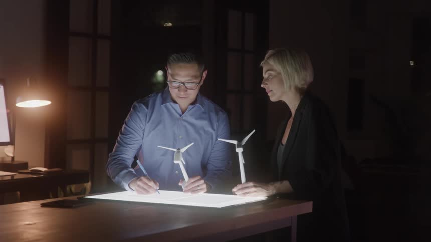A man and woman examine model windmills in the office