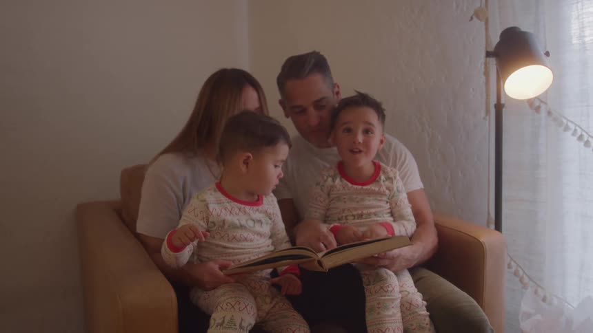 A family of four people sitting together on an armchair and reading a book