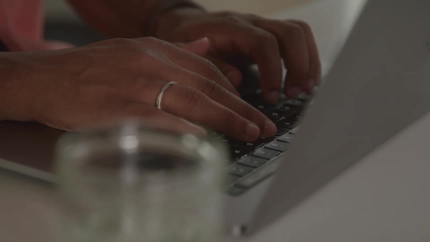 A closeup of a persons hands typing on a laptop