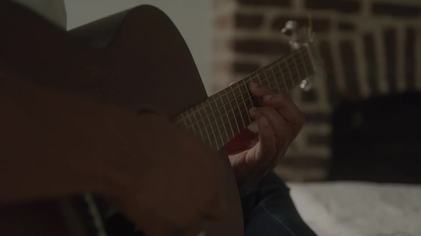 A person sits in the living room playing a guitar
