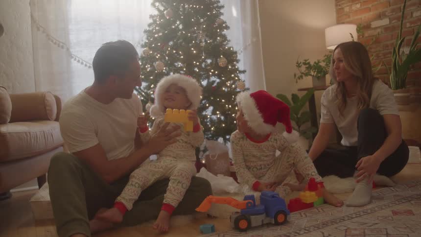 A family gathered in the living room at christmas near a christmas tree a man a woman and two boys with the man holding one of the boys in his arms all happy