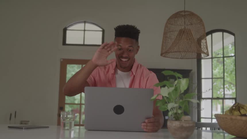 Smiling man waving in front of a laptop