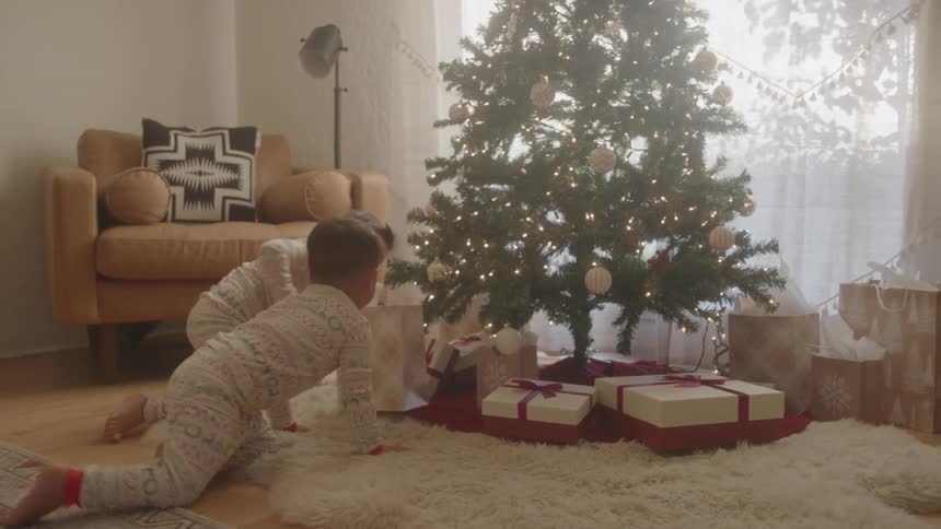 Children excitedly look at christmas presents under a decorated tree