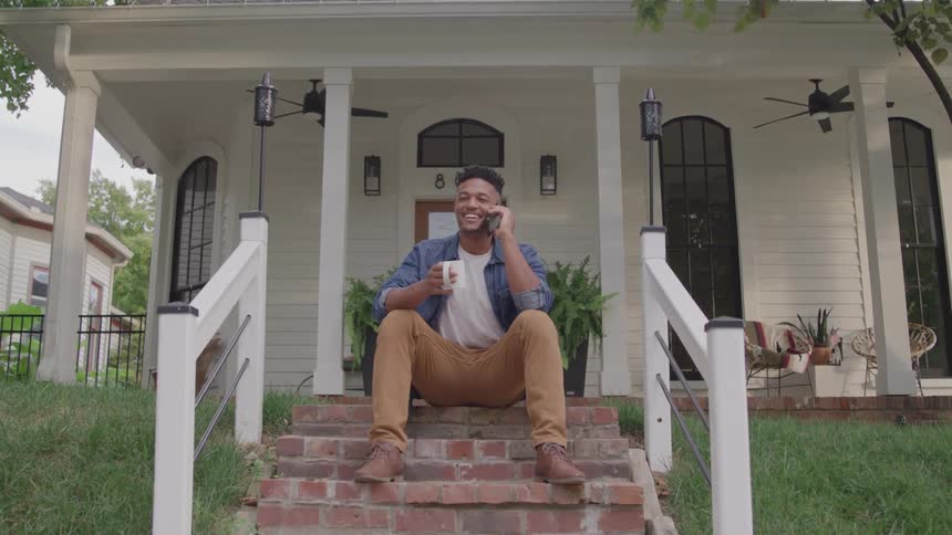 Man sitting on the house steps talking on the phone with a smile