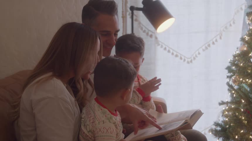 Family gathered on the couch reading a book next to the christmas tree